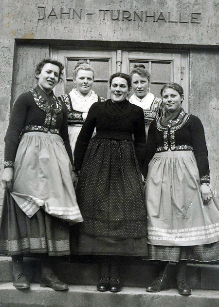 Fünf junge Frauen in Marburger Tracht vor einer Sporthalle in Roßdorf, 1950er Jahre