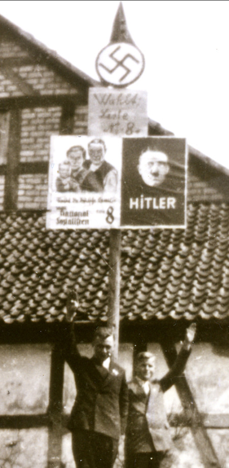 Jugendliche in Haubern stehen unter den Wahlplakaten der NSDAP mit einem Hitlergruß, 1933
